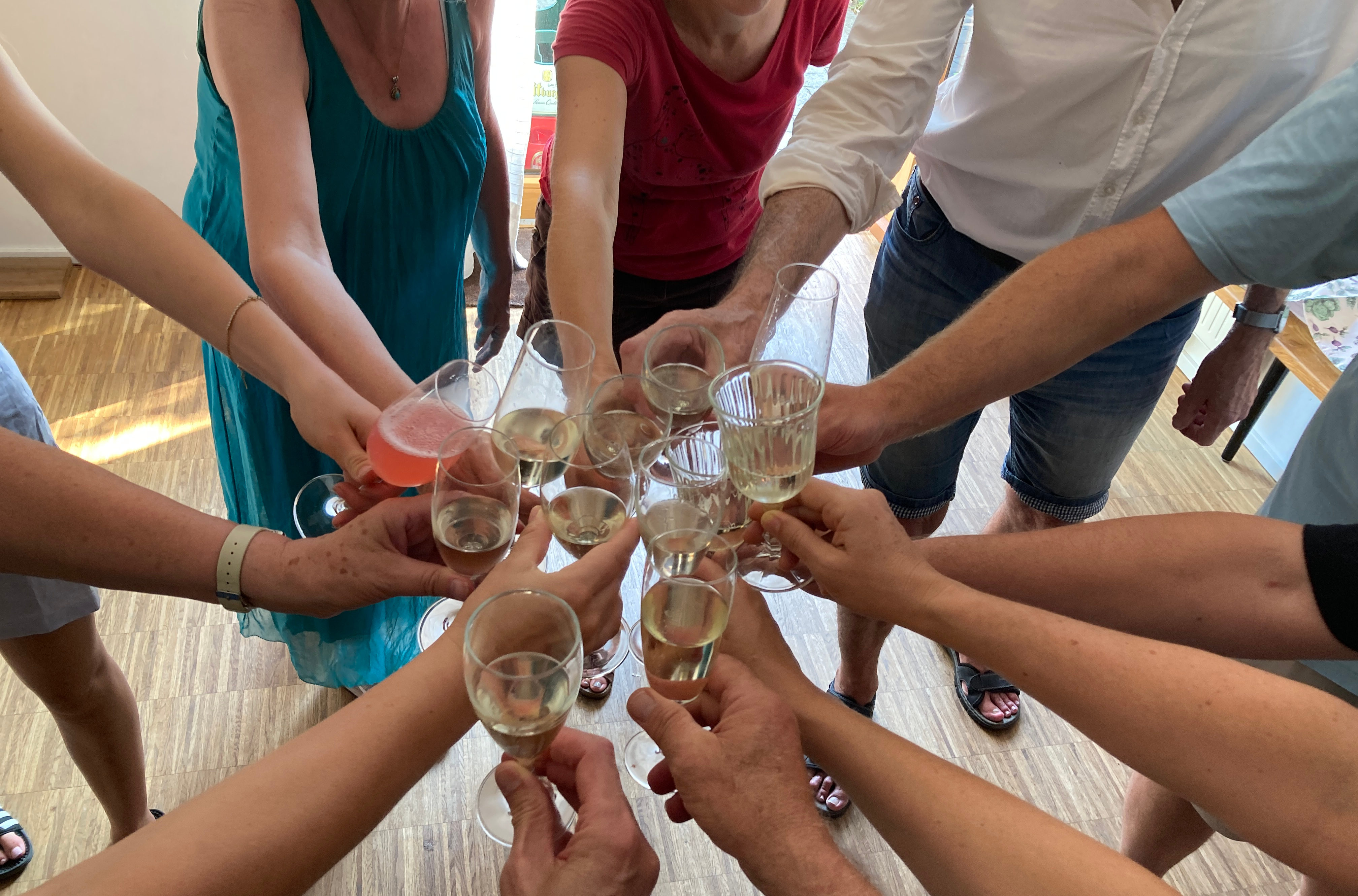 Arme von 12 Menschen, jeweils mit einem Sektglas in der Hand, reichen von außen sternförmig nach innen zum Anstoßen